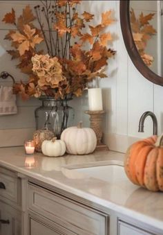 a bathroom counter with candles, pumpkins and flowers on it in front of a mirror