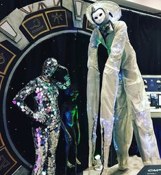 two mannequins dressed as astronauts in front of a clock with the moon behind them