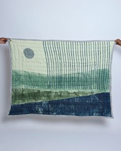 a person holding up a quilt that is made with blue, green and white colors