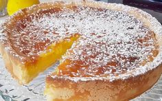 a lemon pie on a glass plate with a slice missing from it and two lemons in the background