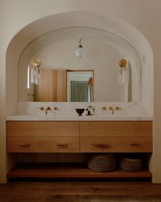 a bathroom vanity with two sinks under a large arched mirror and lights above the sink