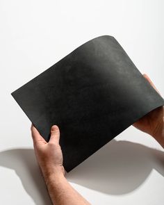 a person holding up a black piece of paper in their hand on a white background