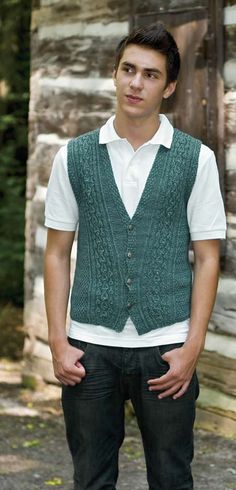 a man standing in front of a log cabin wearing a green vest and white shirt