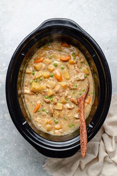 a black crock pot filled with chicken and potatoes next to a white napkin on top of a gray surface