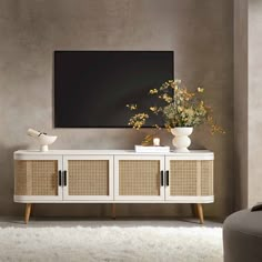 a white entertainment center with wicker doors and two vases filled with yellow flowers