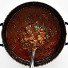 a large pot filled with stew on top of a white counter next to a spoon