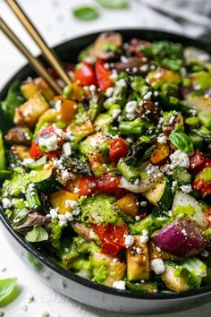 a black bowl filled with vegetables and topped with feta cheese, tomatoes, broccoli, and other veggies