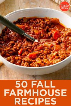 a white bowl filled with chili and meat on top of a wooden table next to bread