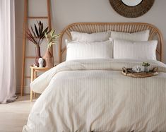 a bed with white linens and pillows in a room next to a mirror, potted plant and wicker basket