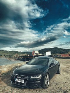 a black car parked on top of a dirt field next to a body of water