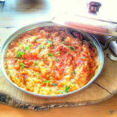 a large metal pan filled with food sitting on top of a wooden table next to a knife