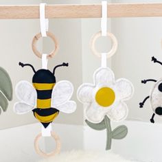 three baby mobiles hanging from a wooden rod with flowers and bees on them,