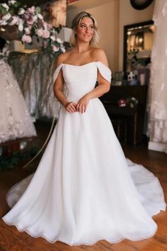 a woman wearing a white wedding dress standing in front of some dresses on the floor