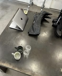 a table with two cups and an apple laptop on it next to a pair of black boots