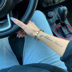 a woman with a tattoo on her arm driving a car and holding the steering wheel