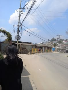 a woman standing on the side of a road next to power lines