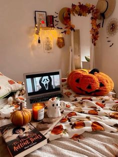 a laptop computer sitting on top of a bed covered in blankets and pumpkins next to candles