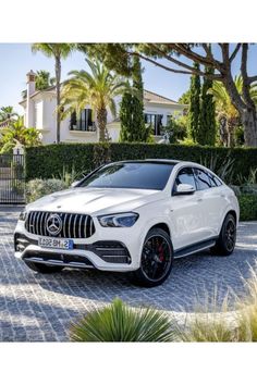 a white mercedes benz suv parked in front of a house with palm trees and bushes