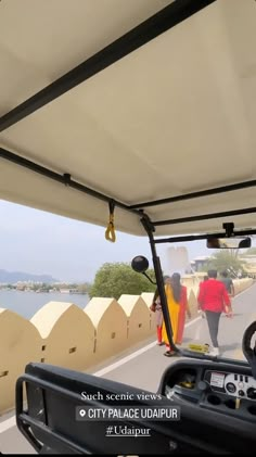 two people walking down the road in a golf cart on a sunny day with blue water behind them