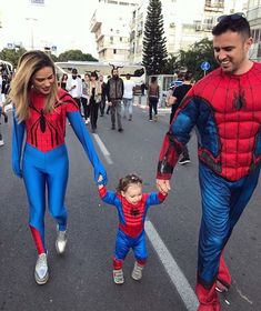 a man and woman in spiderman costumes walking down the street with a small child