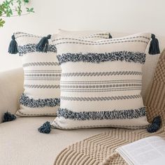 two pillows sitting on top of a couch next to a pillow with tassels