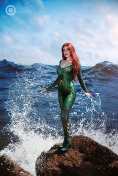 a woman in a green bodysuit standing on top of a rock near the ocean