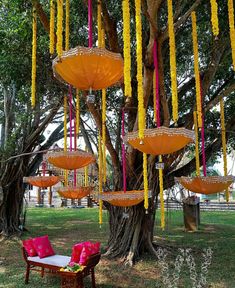 an outdoor seating area with yellow umbrellas hanging from the trees and pink pillows on the ground