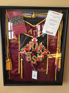 a graduation cap and gown hanging in a black framed case with tassels on it