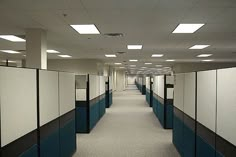 an empty office hallway with blue and white partitions on the walls, along with several cubicles