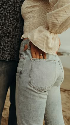 a man and woman standing next to each other on the beach with their hands in their pockets