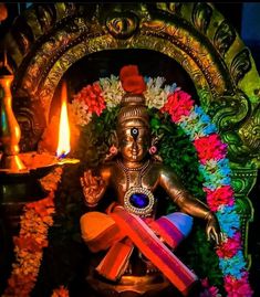 the statue is surrounded by colorful flowers and candles in front of a lit candle holder