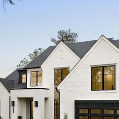 a white brick house with black garage doors and two story windows on the top floor