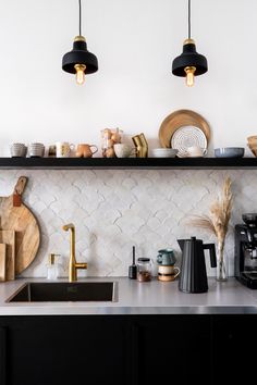 a kitchen with black cabinets and white tile backsplash, hanging lights above the sink