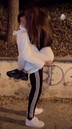 a woman in white jacket and black leggings standing next to wall with graffiti on it