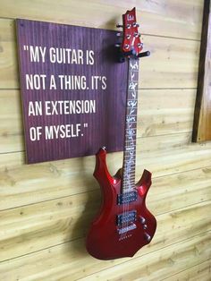 a red guitar hanging on the wall next to a sign that says, my guitar is not a thing it's an extension of myself