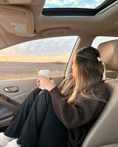 a woman sitting in the back seat of a car holding a coffee cup and looking out the window