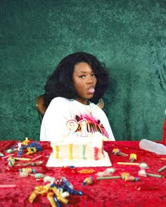 a woman sitting at a table with a birthday cake in front of her and other decorations on the table