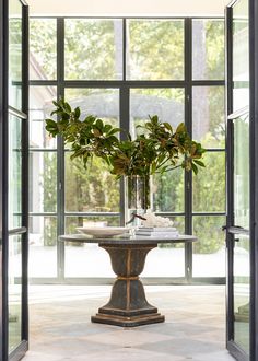 a vase filled with plants sitting on top of a table next to an open door