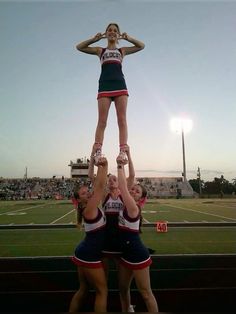 two cheerleaders are doing tricks on the sidelines at a football game while another girl is holding her hands up in the air