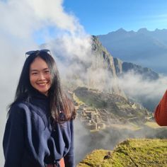 two women standing on top of a mountain with clouds in the sky behind them and one woman smiling at the camera