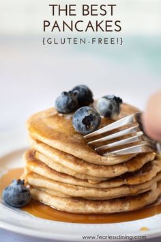 stack of pancakes with blueberries on top and syrup being drizzled over them