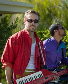 a man in red jacket and sunglasses holding an accordion with two other men behind him