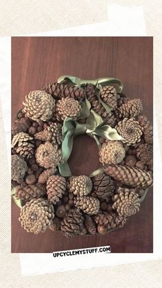 a wreath made out of pine cones and green ribbon on top of a wooden table