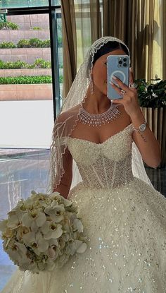 a woman in a wedding dress taking a selfie with her cell phone while holding a bouquet