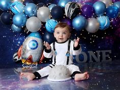 a baby sitting on the floor in front of some balloons and space themed backdrops