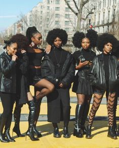 the models are posing together on the sidewalk in their black outfits and boots, all looking at their cell phones