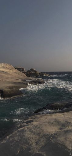 the water is very choppy and blue with waves coming in from the rocky shore