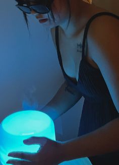 a woman in black dress holding a blue light up bowl with her hands on it