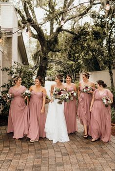 a bride and her bridesmaids standing together in front of a tree with their bouquets