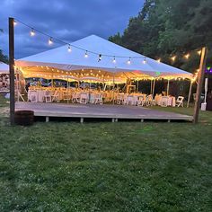 a large tent set up with tables and chairs for an outdoor wedding reception at dusk